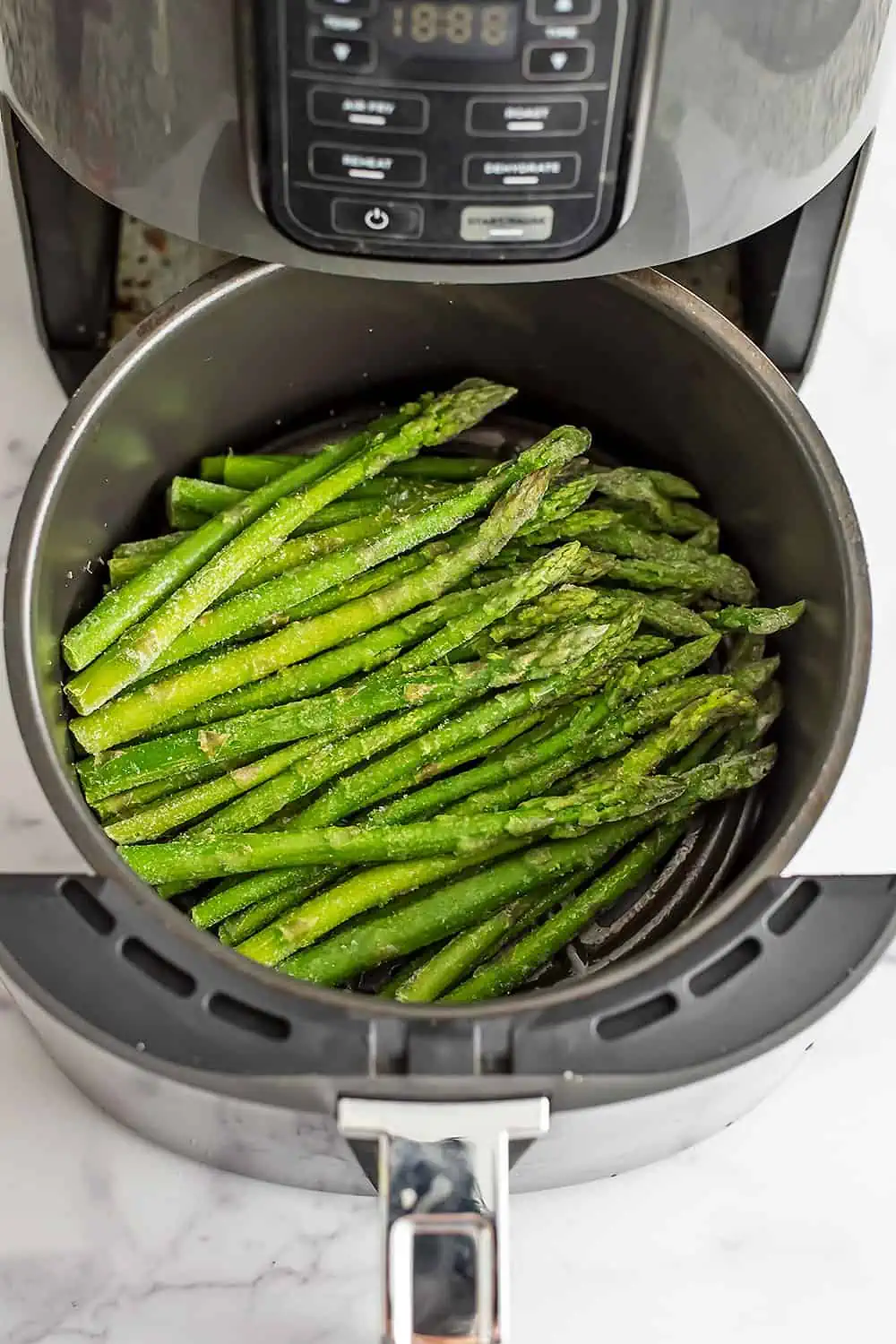 Frozen asparagus in air fryer basket before cooking.