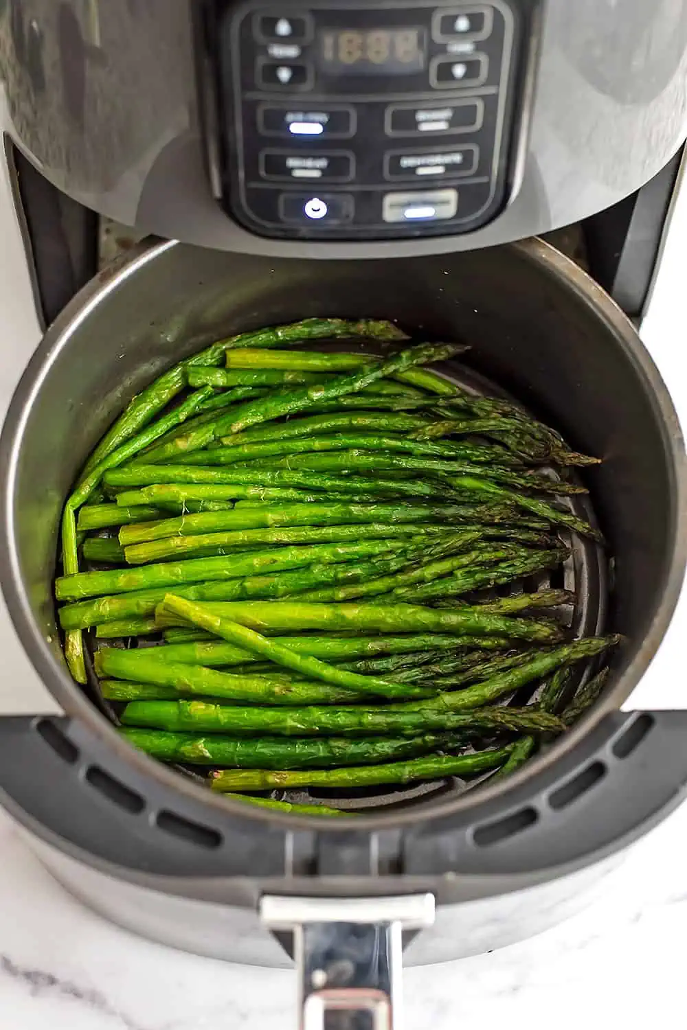 Cooked frozen asparagus in an air fryer basket.