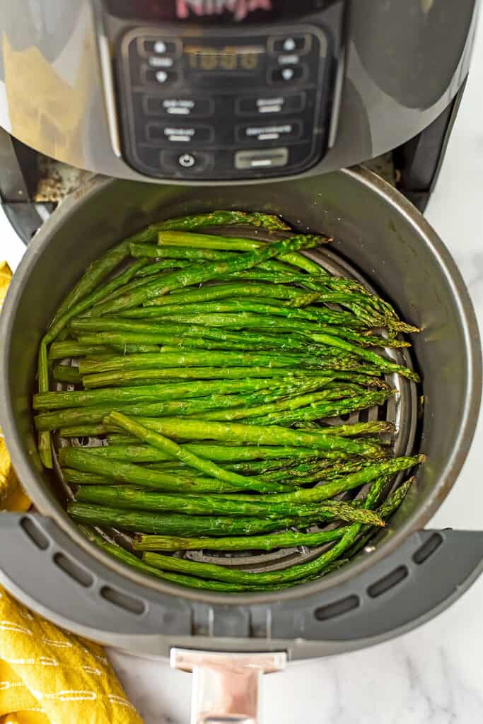 Perfectly cooked asparagus in the air fryer basket with yellow napkin on the side.  