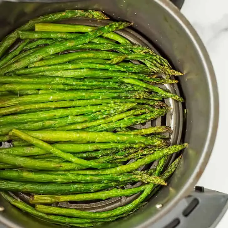 Cooked frozen asparagus in an air fryer basket.