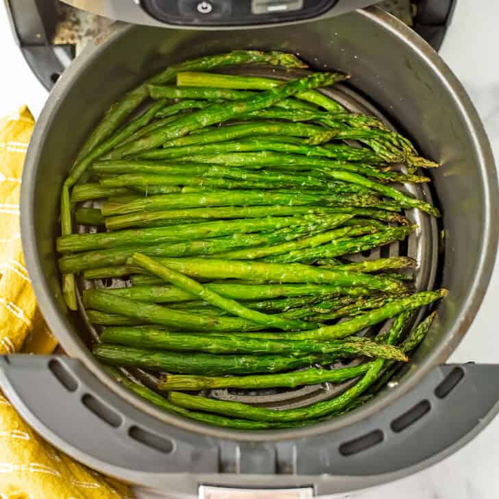 Cooked asparagus in air fryer basket with yellow napkin on the side.