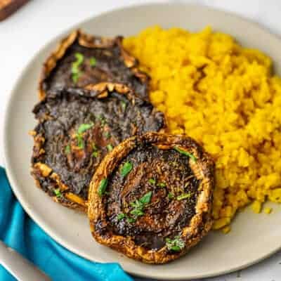 Three portobello mushrooms on a plate with yellow rice.