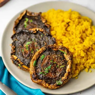Three portobello mushrooms on a plate with yellow rice.