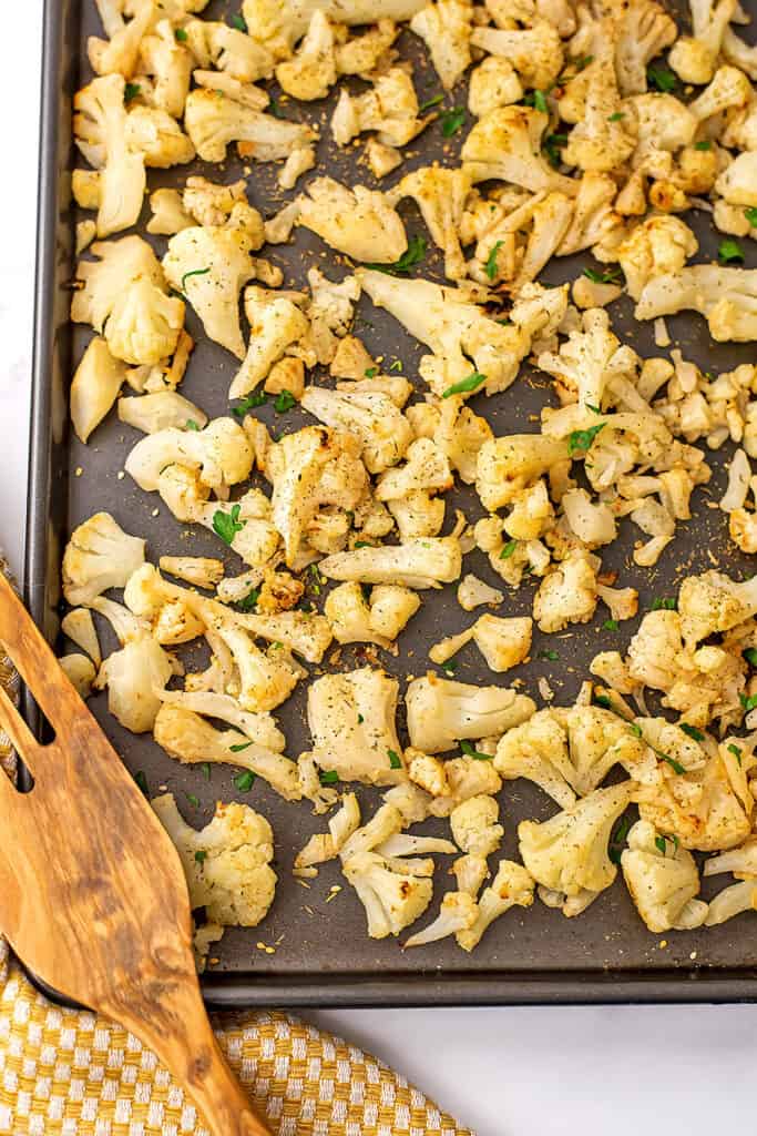 Baked frozen cauliflower on a baking sheet with wood spatula on the side. 