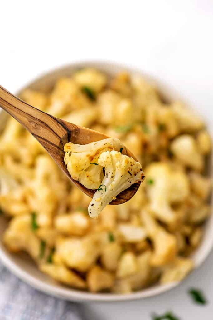 Wood spoon holding roasted cauliflower over a bowl.