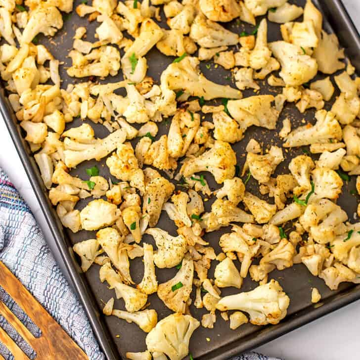Roasted frozen cauliflower on a baking sheet with a blue napkin on the side.