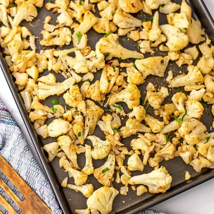 Roasted frozen cauliflower on a baking sheet with a blue napkin on the side.