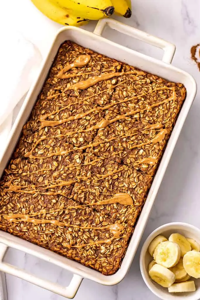 Large casserole dish filled with banana baked oatmeal with peanut butter drizzled on top.