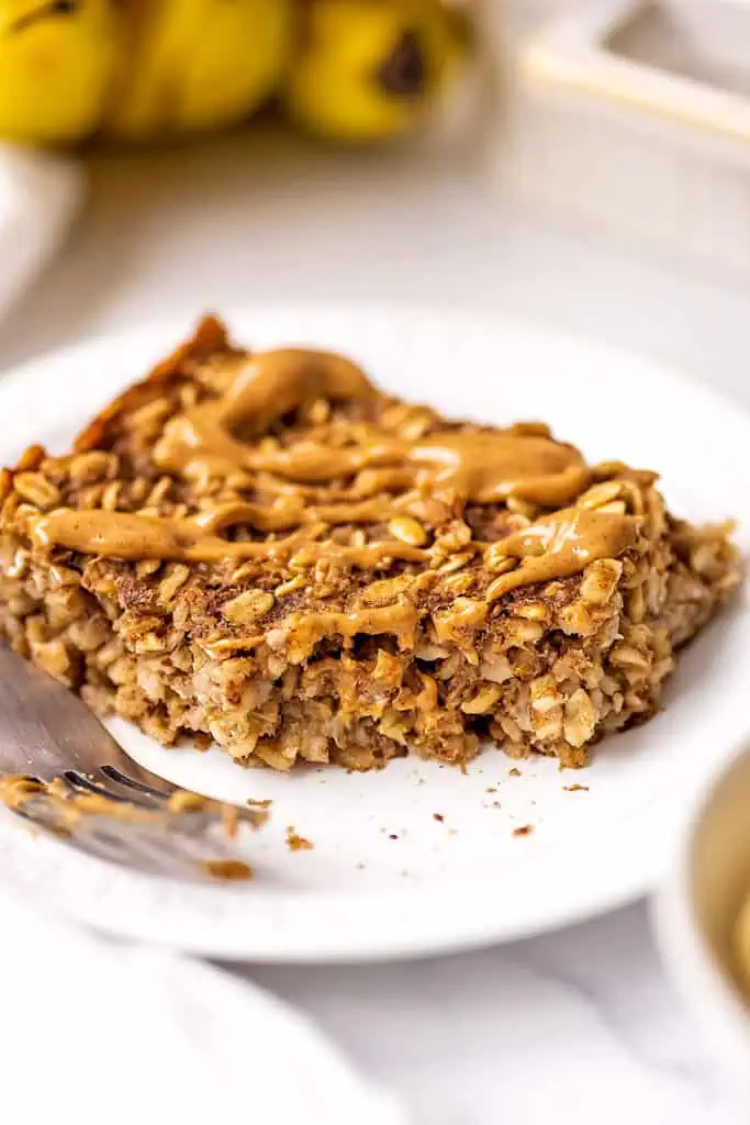 Peanut butter drizzled over a slice of banana bread baked oats with a bite taken out.