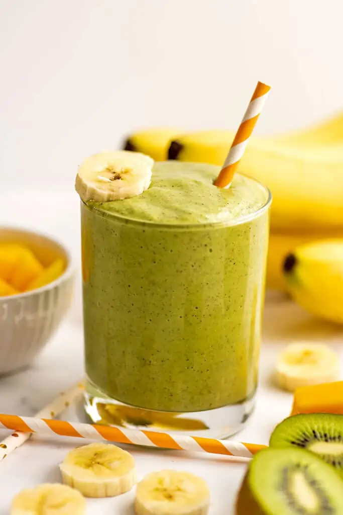 Banana mango kiwi smoothie in a small glass with sliced bananas on top.
