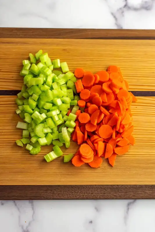 Chopped carrots and celery on wood cutting board.