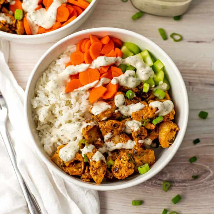 Buffalo chicken rice bowl with carrots and celery, ranch dressing on top.