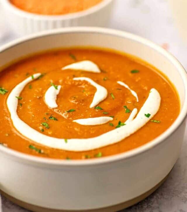 Red lentil and red pepper soup in a bowl with drizzle of cashew cream.