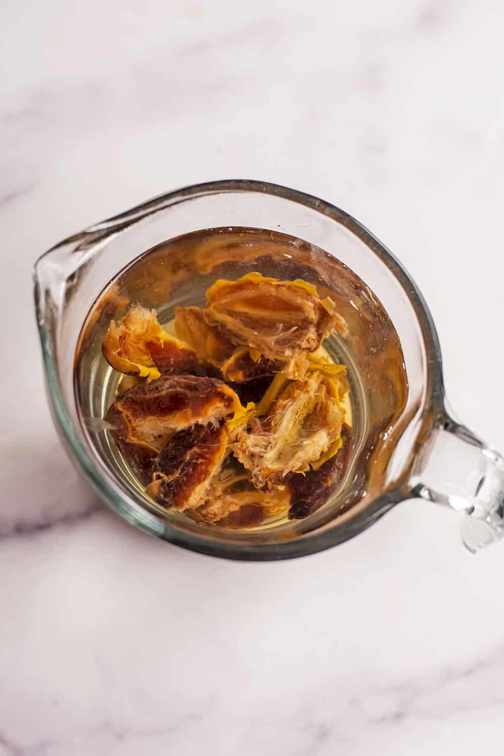 Pitted dates soaked in hot water in glass measuring cup.