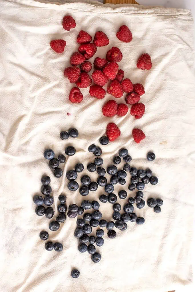Raspberries and blueberries on a paper towel drying after being washed.