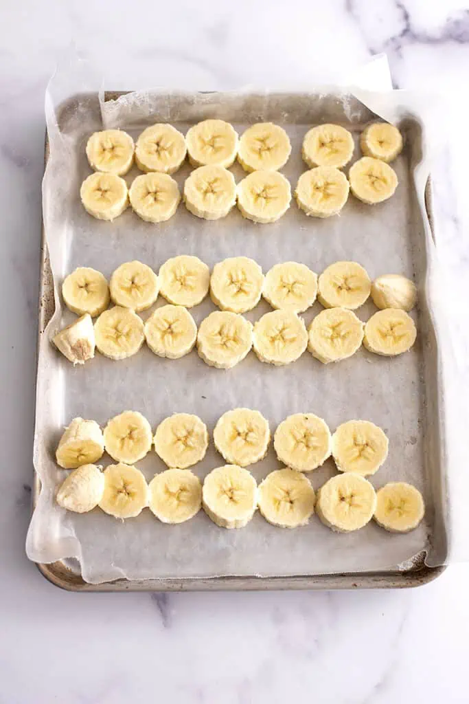 Frozen banana slices on a baking sheet with wax paper.