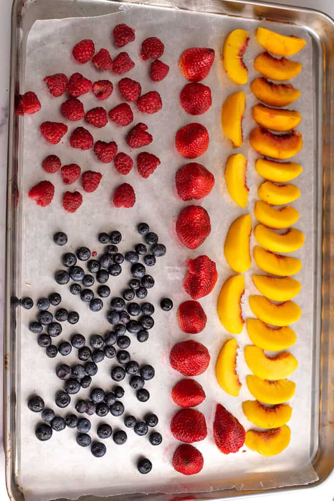 Frozen berries and stone fruit on a backing sheet.