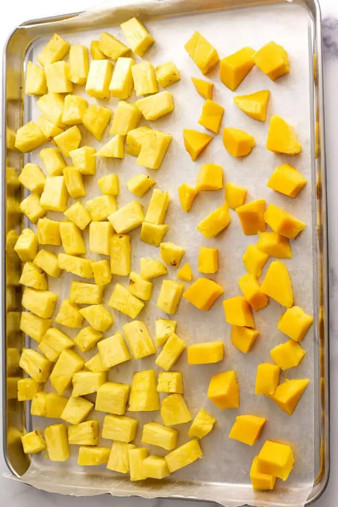 Frozen mangos and pineapple cubes on a baking sheet.
