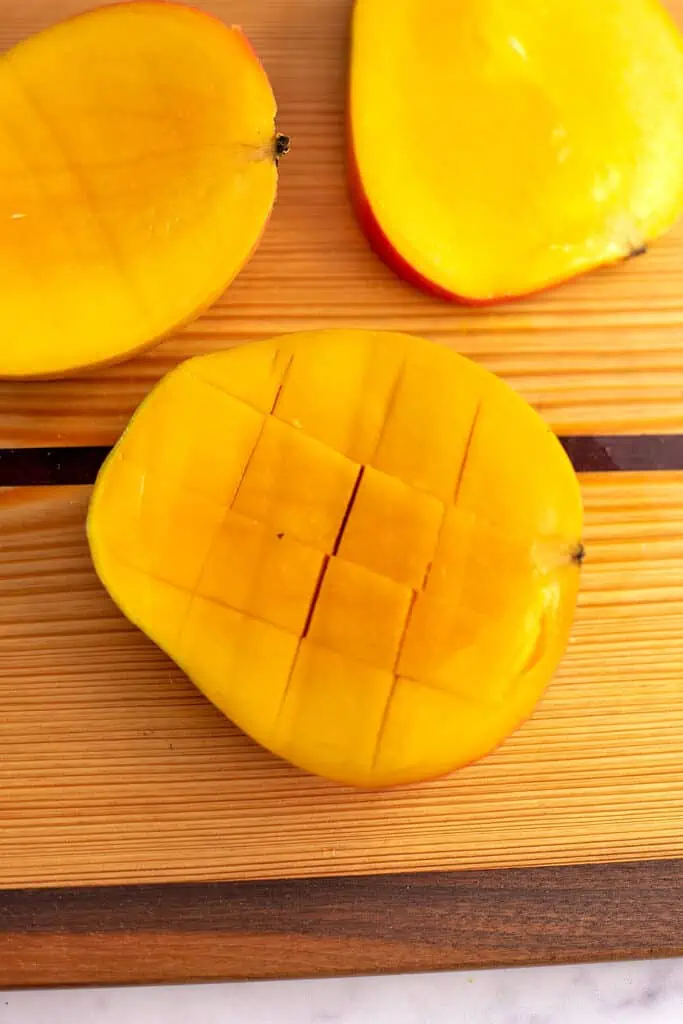 A mango on a cutting board being cut into cubes.
