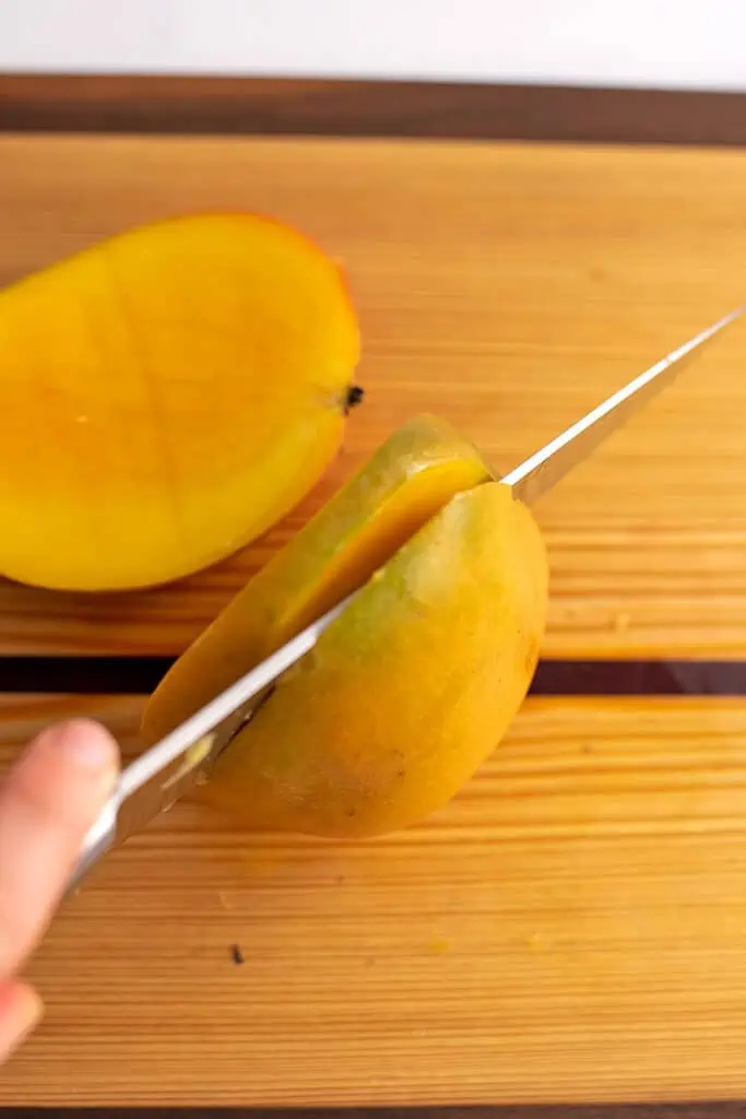 A mango on a cutting board being cut into slices.