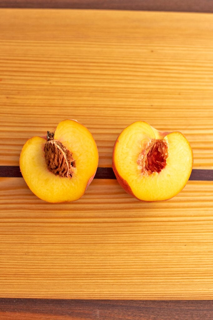 Peach with the skin removed and cut in half showing the pit on a cutting board.