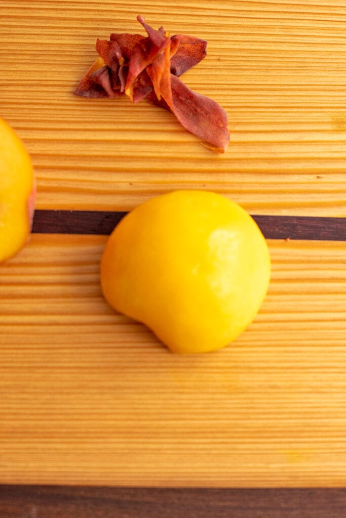 A preach cut in half sliced side down on the cutting board.