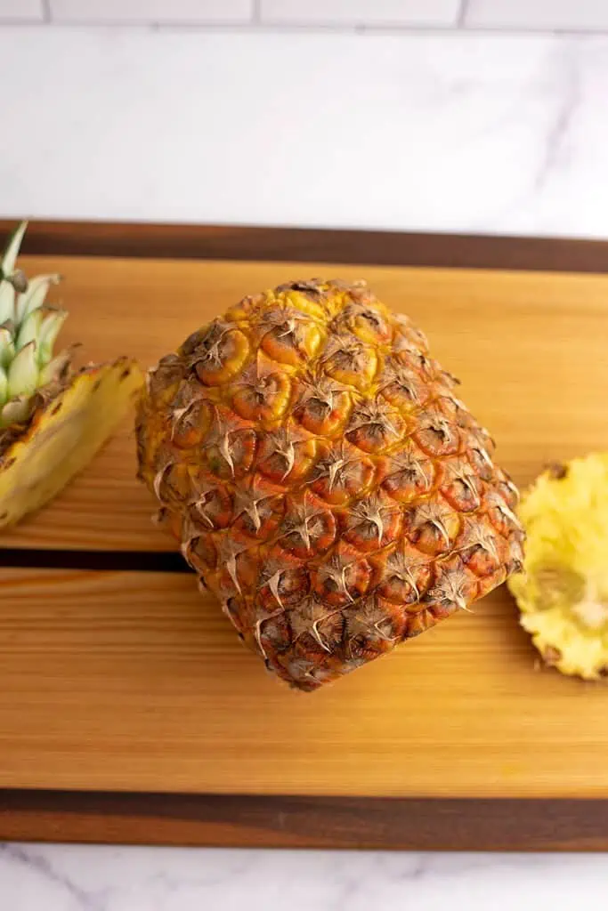 A whole pineapple with it's top cut off sitting on a cutting board.