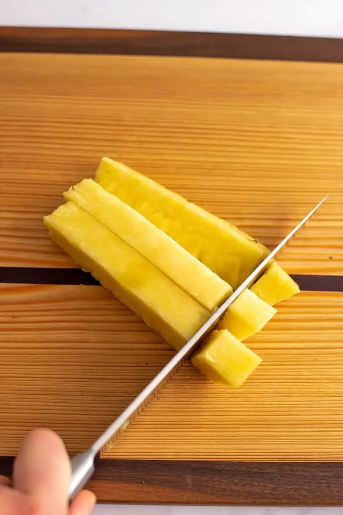 A pineapple on a cutting board being cut into cubes. 