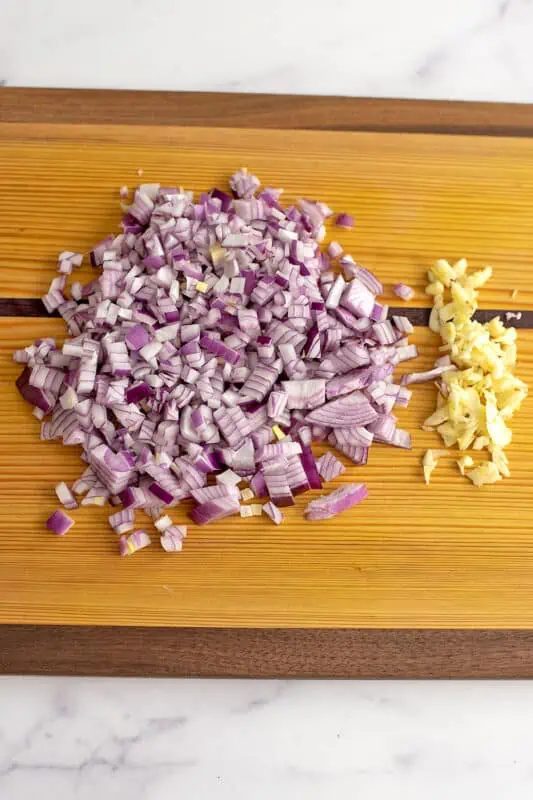 Chopped red onion and sliced garlic on wood cutting board.