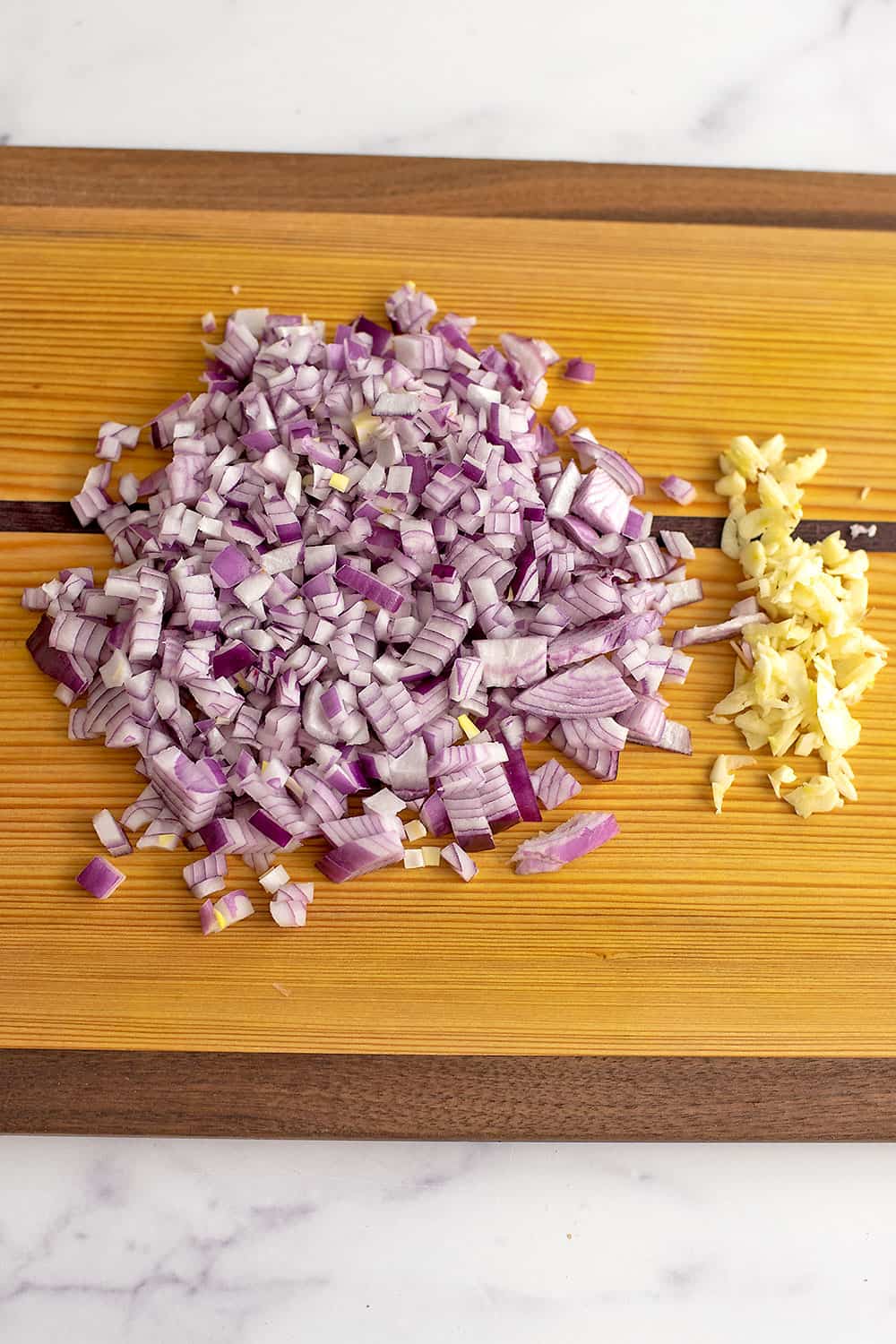 Chopped red onion and sliced garlic on wood cutting board. 