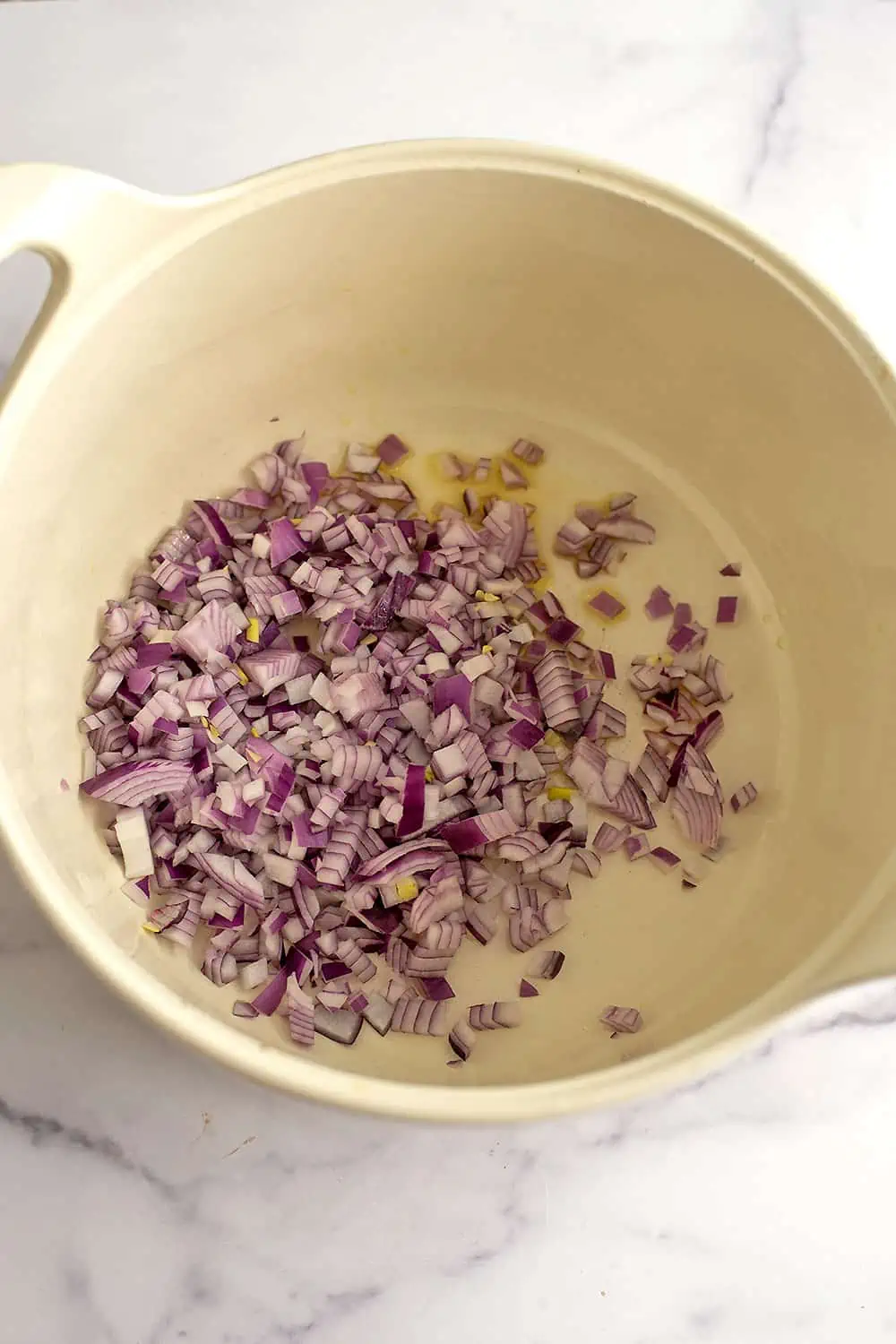 Chopped red onion in a large enameled pot.