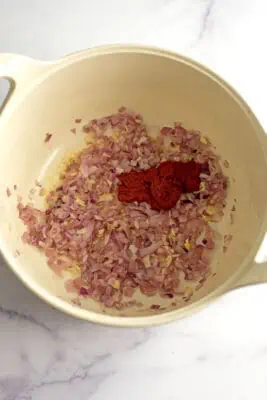 Tomato paste in pot with cooked red onions and garlic.
