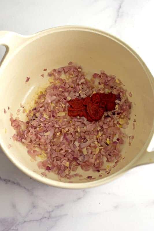 Tomato paste in pot with cooked red onions and garlic.