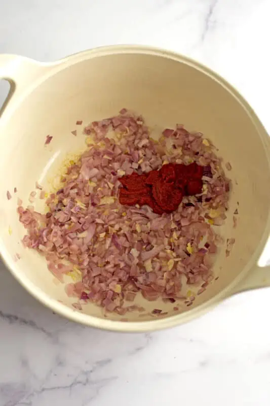 Tomato paste in pot with cooked red onions and garlic.