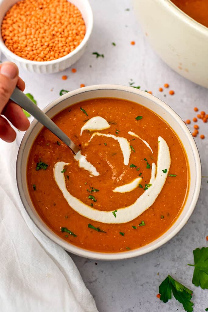 Spoon in a bowl of red pepper lentil soup with cashew cream sauce.
