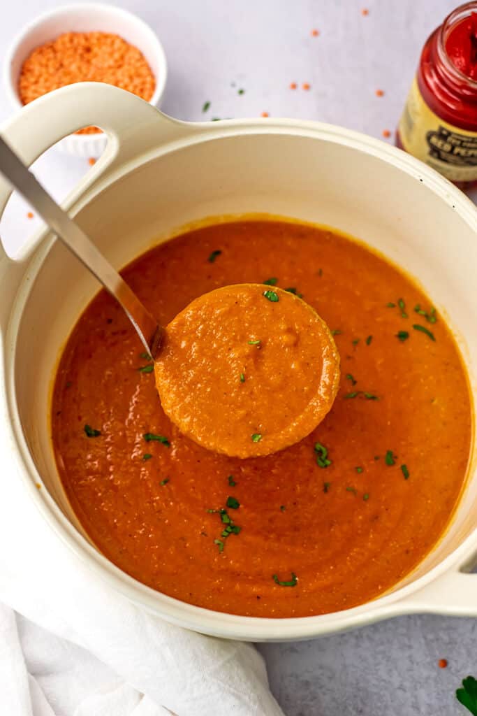 Silver ladle picking up lentil and red pepper soup from the pot.