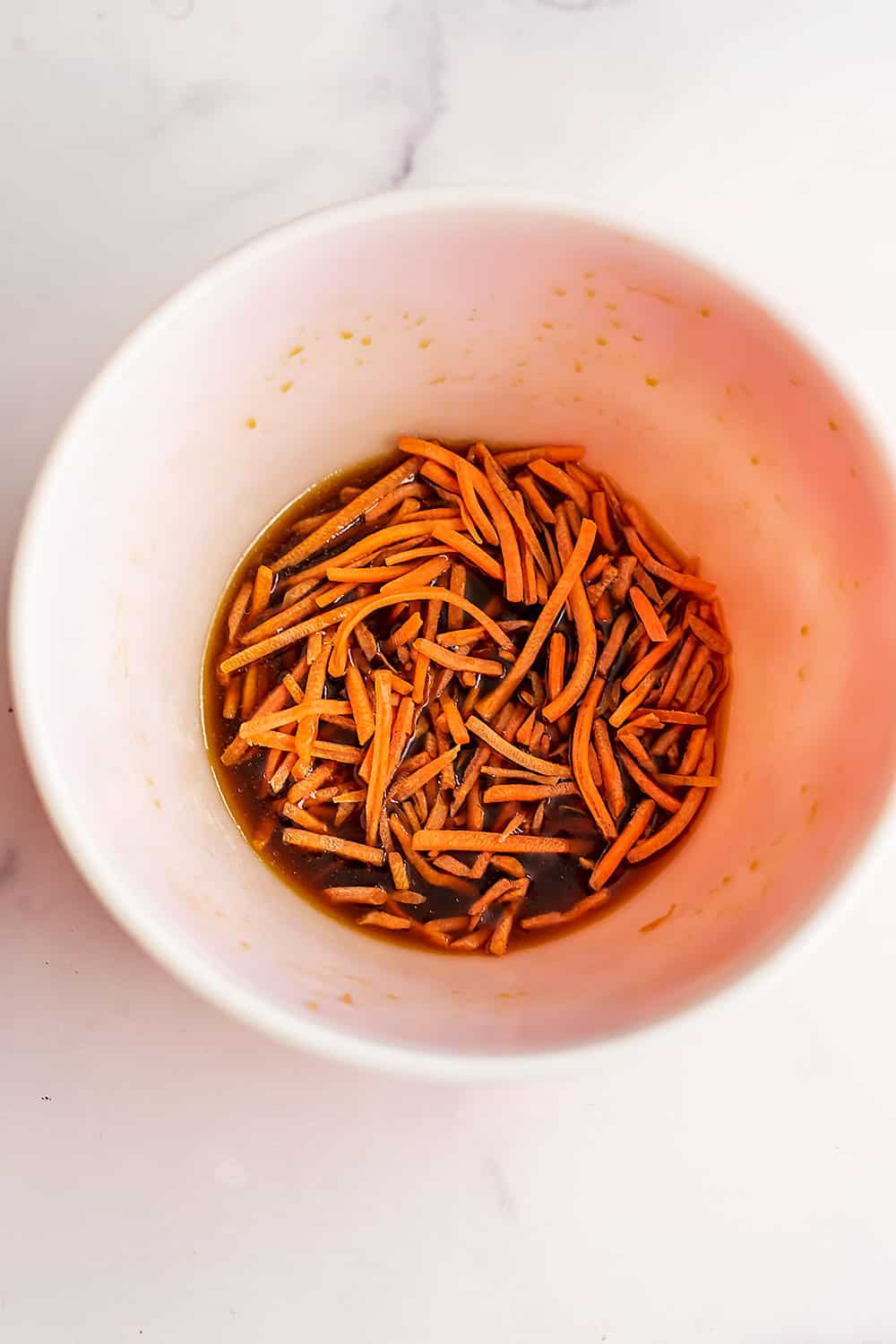 Shredded carrots in bowl with marinade.