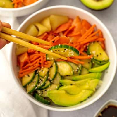 Cucumber and shredded carrots being picked up by chopsticks.