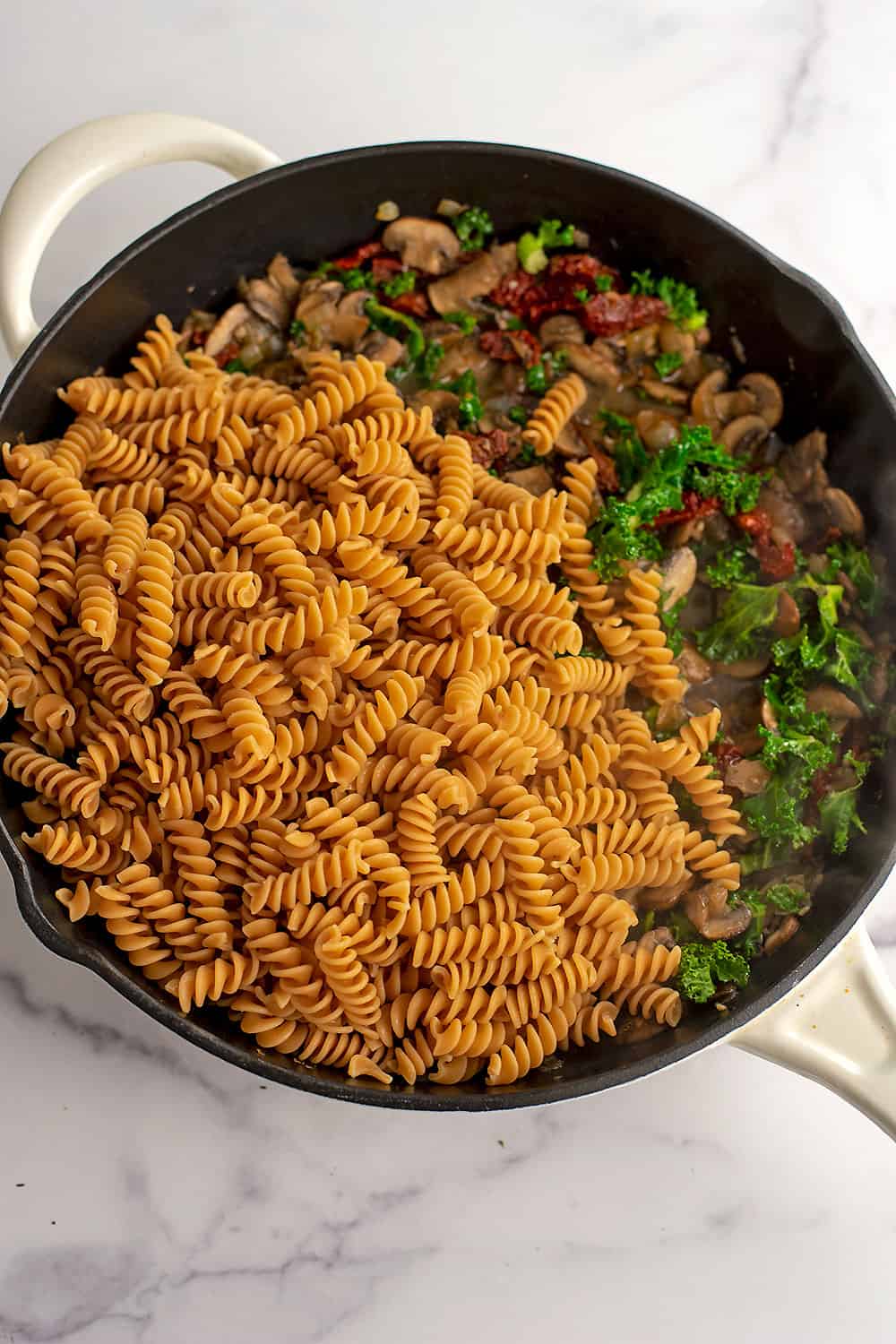 Cooked pasta added to skillet with mushrooms, sundried tomatoes and kale.