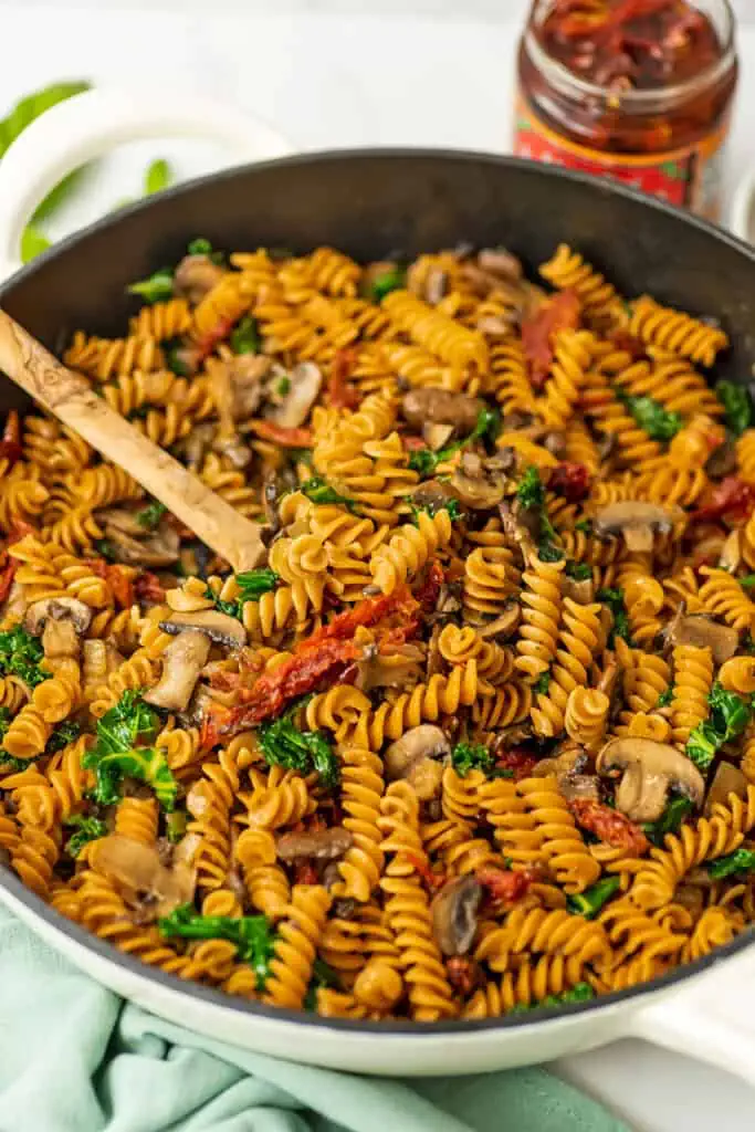 Wooden spoon in a skillet with mushroom sundried tomato pasta.