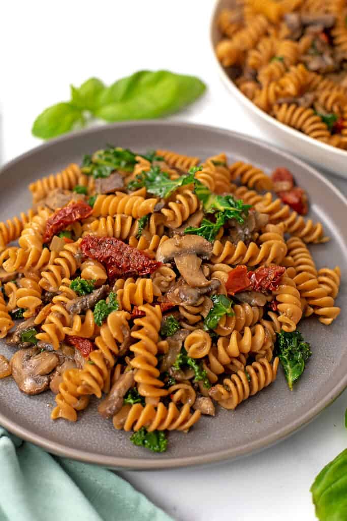 Sundried tomato mushroom pasta on a grey plate with green napkin on the side.