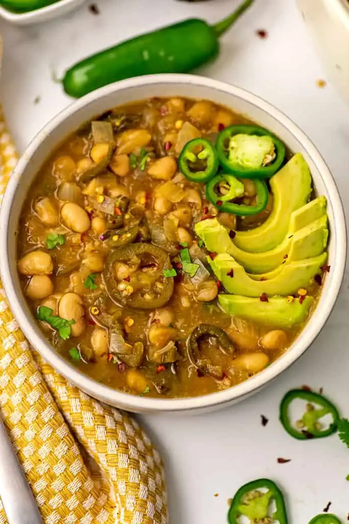 Large bowl filled with vegan green chili, sliced avocado on top.