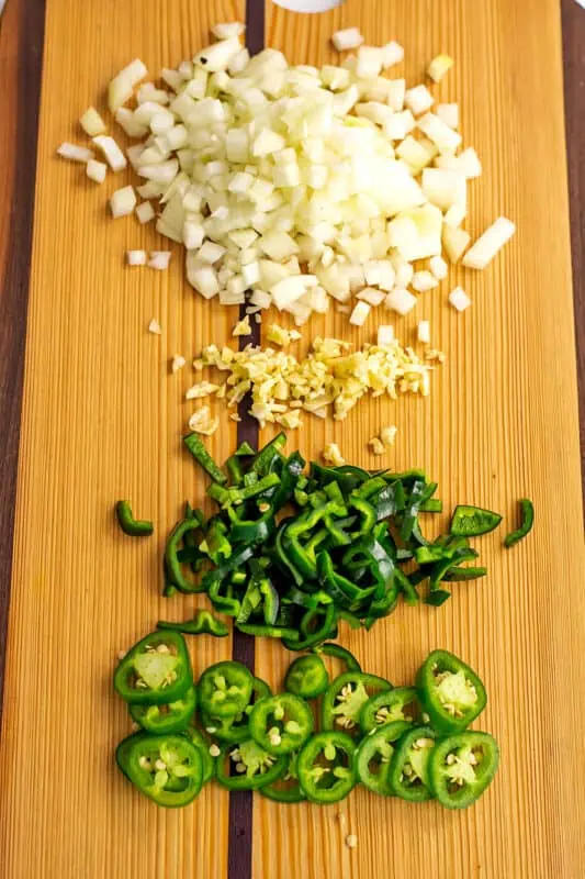 Chopped onion, garlic, poblano peppers and jalapeno on a wood cutting board.