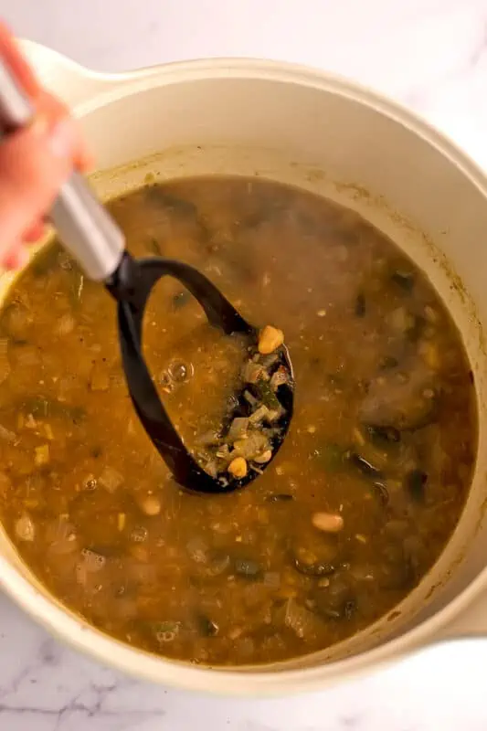 Potato masher mashing some of the beans in the chili pot.