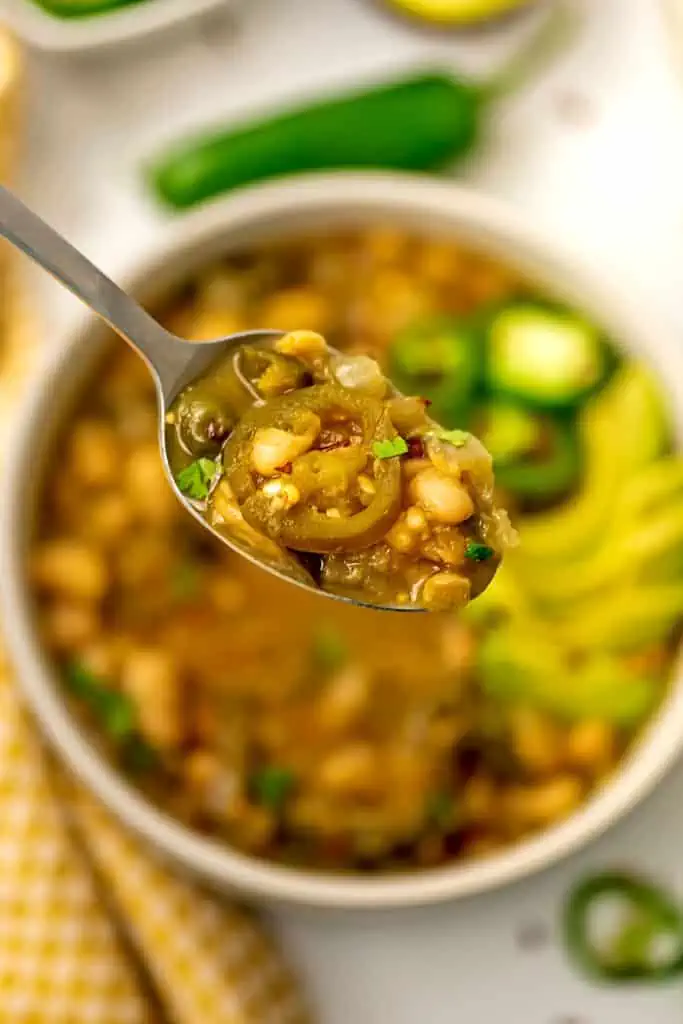 Spoonful of vegan green chili being held over the bowl.