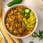 Vegetarian green chili in a white bowl with a yellow napkin on the side.