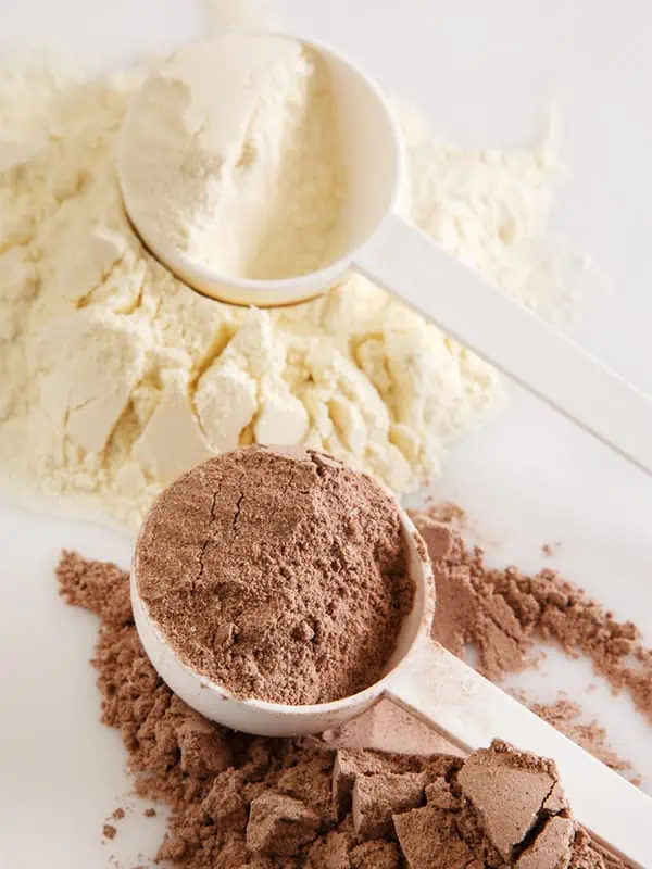 Chocolate and vanilla protein powder spilled out on a table with the powder scoopers sitting next to the spilled protein powder.