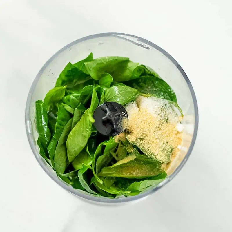 Small food processor filled with basil, lemon juice and spices. 