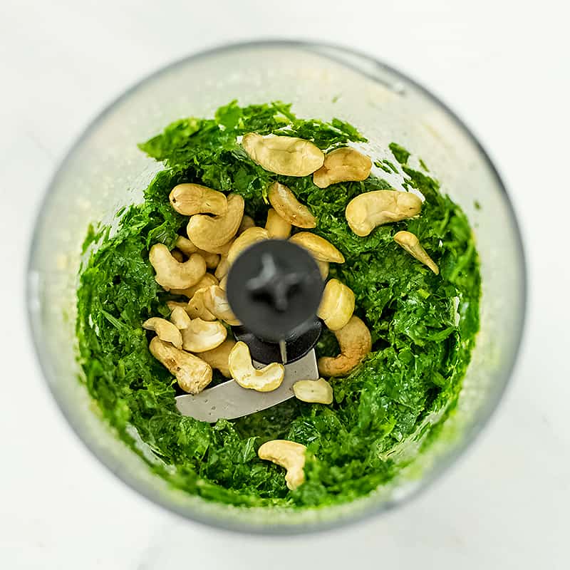 Cashews added to food processor with basil mixture.