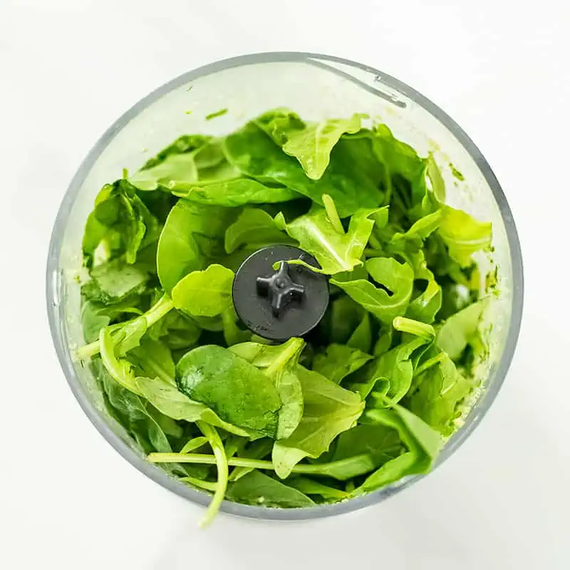 Spinach and arugula added to small food processor.